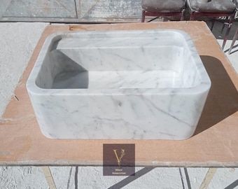 May include: A white marble sink with a rectangular shape. The sink is sitting on a wooden surface.