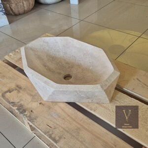 May include: A light beige stone sink with a hexagonal shape. The sink is sitting on a wooden pallet.