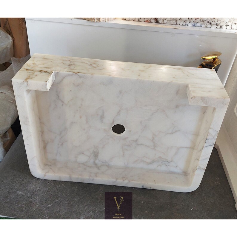 May include: White marble bathroom sink with a round drain hole. The sink is rectangular and has a slightly curved edge.