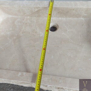 May include: A white marble sink with a drain hole and a measuring tape next to it. The sink is 48 inches long.