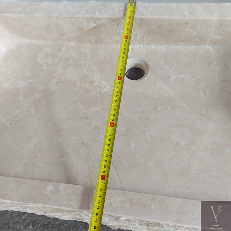 May include: A white marble sink with a drain hole and a measuring tape next to it. The sink is 48 inches long.