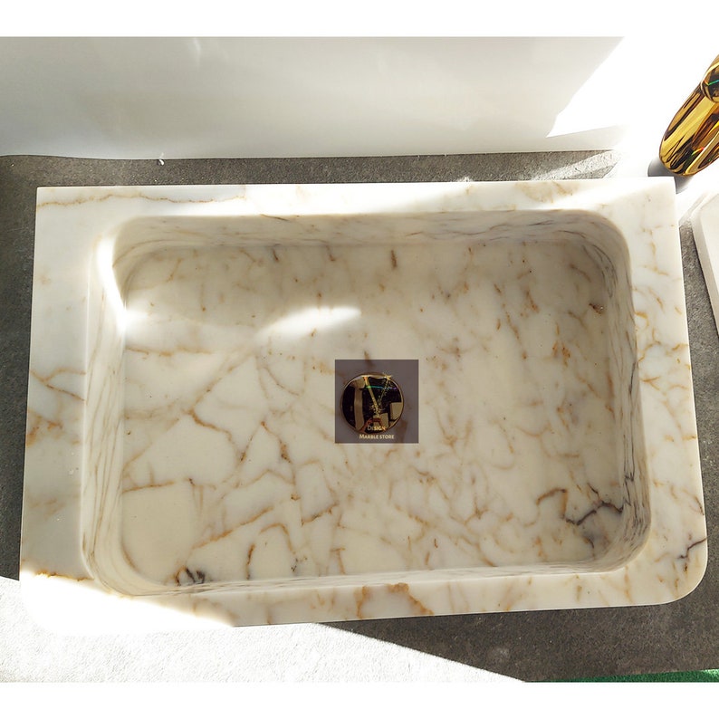 May include: A white marble sink with gold veining. The sink is rectangular and has a rounded edge. The sink is set into a white countertop.