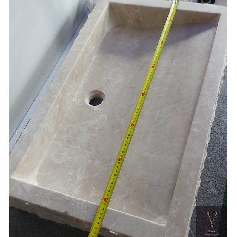 May include: A rectangular, off-white marble sink with a single drain hole. The sink is being measured with a tape measure, which shows it is 58 inches long.
