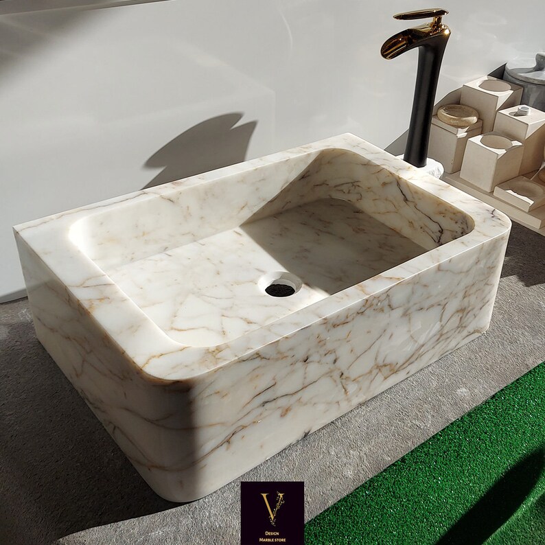 May include: A white marble bathroom sink with a rectangular shape and rounded edges. The sink has a drain hole and is designed for wall mounting.