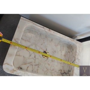 May include: A white marble sink with a gold drain stopper. The sink is 30 inches wide.