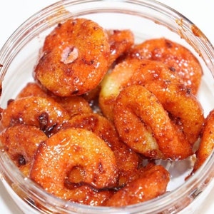 Puede incluir: Un tarro de vidrio lleno de pequeños agujeros de donut redondos, de color marrón dorado y glaseados.