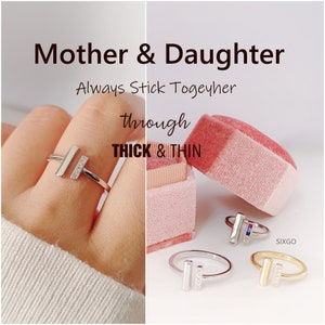 May include: Two silver rings with a vertical bar design and small clear stones. The rings are in a pink box with the text "Mother & Daughter Always Stick Together Through Thick & Thin".