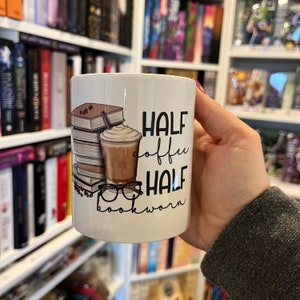 Könnte beinhalten: Weiße Keramiktasse mit einer Grafik eines Stapels Bücher, einer Tasse Kaffee und einer Brille. Der Text auf der Tasse lautet "Half coffee half bookworm".