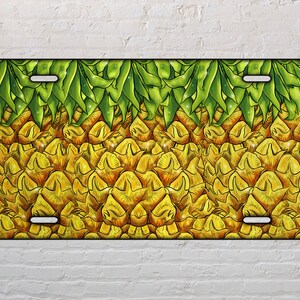 May include: A yellow and green pineapple design on a license plate. The pineapple is depicted in a cartoon style with a detailed texture.