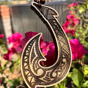 May include: A wooden fish hook pendant featuring intricate laser-engraved tribal patterns in dark brown tones. The pendant is suspended from a cord adorned with round, dark brown wooden beads, creating a cohesive and detailed accessory piece.