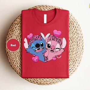 A red t-shirt with a cartoon image of two cartoon characters, one blue and one pink, along with heart-shaped symbols and the text "I love you".