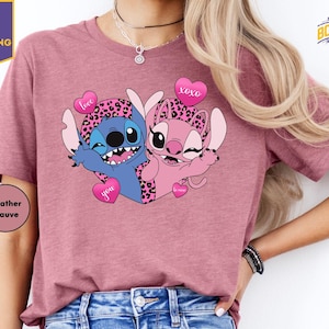A woman wearing a pink t-shirt with a graphic of two cartoon characters, one blue and one pink, holding hearts and smiling.