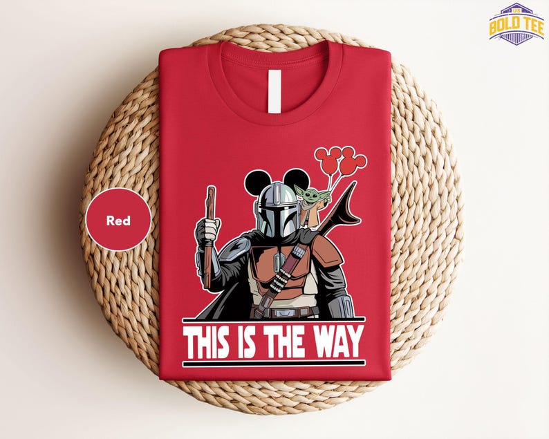 A red t-shirt with a graphic design depicting a character from the Star Wars franchise, holding a gun and a balloon, along with the text "THIS IS THE WAY".