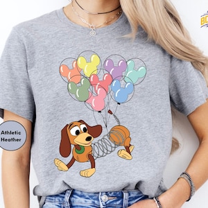 a woman wearing a shirt with a cartoon dog holding a bunch of balloons