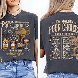 May include: A charcoal gray t-shirt featuring a graphic print of various alcoholic beverages with mouse-ear accessories and the text I'M MAKING POUR CHOICES AROUND THE WORLD. The back design includes a list of countries and their respective toasts.