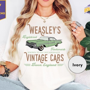 May include: Ivory-colored t-shirt featuring a green vintage car graphic with the text "WEASLEY'S Registered Trademark VINTAGE CARS Devon. England." The shirt has a crew neck and short sleeves. A "NEXT DAY SHIPPING" label is visible.