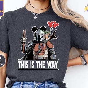 A person wearing a gray t-shirt with a graphic design depicting a character from the Star Wars franchise, holding a balloon and a peace sign.