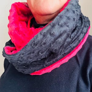 May include: A black and pink reversible neck warmer made of soft, plush fabric. The warmer is folded in half, showing both sides.