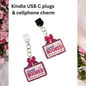 May include: Two rectangular acrylic charms attached to USB-C plugs via silver-toned metal jump rings. Each charm features a pink border, a red bow at the top, and the text Sorry! I AM BOOKED Please leave me alone in red and purple lettering.