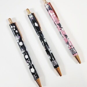 May include: Three retractable pens with rose gold clips and tips. Two pens feature a black glittery barrel with white cloud patterns and cartoon character graphics. One pen features a pink glittery barrel with cartoon character graphics and the text ROM.