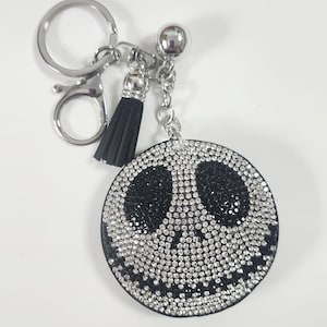 Puede incluir: Un llavero redondo con un dise&ntilde;o negro y plateado. La cara es un c&iacute;rculo negro con un dise&ntilde;o de Jack Skellington, incrustado con brillantes pedrer&iacute;a. Tiene una borla plateada y un llavero plateado.