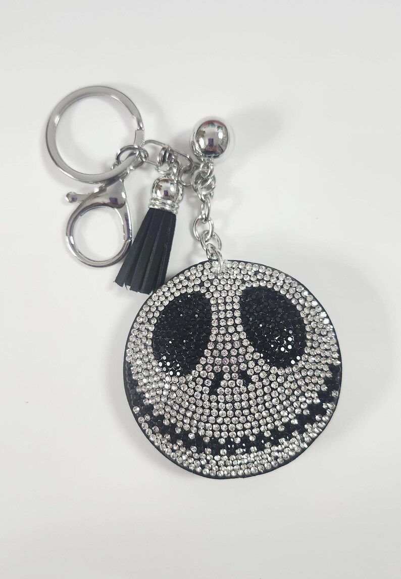 Puede incluir: Un llavero redondo con un dise&ntilde;o negro y plateado. La cara es un c&iacute;rculo negro con un dise&ntilde;o de Jack Skellington, incrustado con brillantes pedrer&iacute;a. Tiene una borla plateada y un llavero plateado.