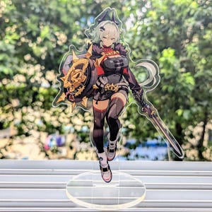 Könnte beinhalten: Ein transparenter Acryl-Ständer mit einer schwarz-weißen Anime-Figur, die ein Schwert und einen Schild hält. Die Figur hat grünes Haar und trägt ein schwarz-rotes Outfit.