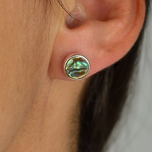 Könnte beinhalten: Ein Paar silberne Ohrstecker mit einem runden Einlegeteil aus Abalone-Muschel. Die Muschel hat ein grün-blau-goldenes, irisierendes Muster.