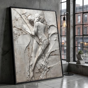 Puede incluir: Una obra de arte enmarcada que presenta una escultura en relieve de mármol blanco de dos figuras abrazándose. La escultura está sobre un fondo texturizado con grietas y líneas visibles. El marco es negro.