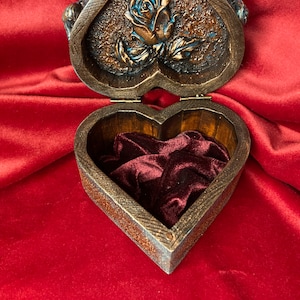 May include: A heart-shaped wooden box with a carved rose design on the lid. The box is open, revealing a red velvet interior.