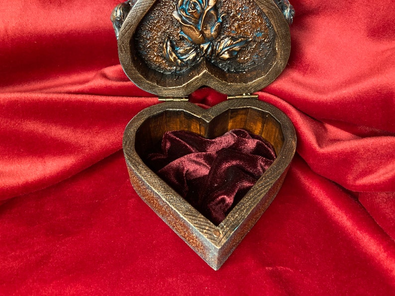 May include: A heart-shaped wooden box with a carved rose design on the lid. The box is open, revealing a red velvet interior.