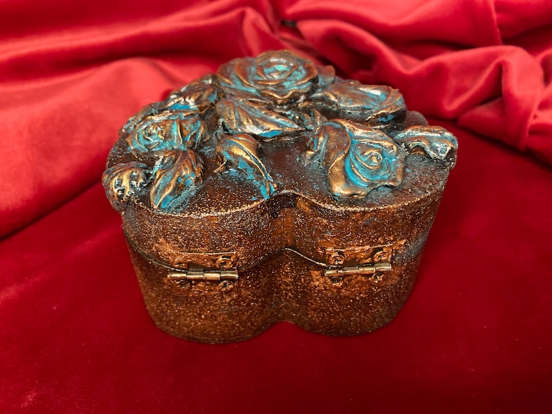 May include: A heart-shaped wooden box with a hinged lid, decorated with blue and gold roses. The box is perfect for storing small treasures or jewelry.