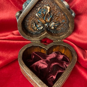 May include: A heart-shaped wooden box with a carved rose design on the lid. The box is open, revealing a red velvet interior.