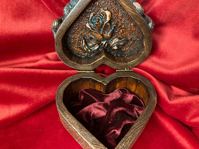 May include: A heart-shaped wooden box with a carved rose design on the lid. The box is open, revealing a red velvet interior.