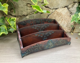 May include: A dark brown wooden letter holder featuring three tiered compartments. The front panel is decorated with embossed scrollwork and a central lion head door knocker motif, finished with dark green accents on the ornate metal feet.