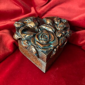 May include: A heart-shaped box with a detailed floral design. The box is made of a dark brown material and features a rose with blue accents.