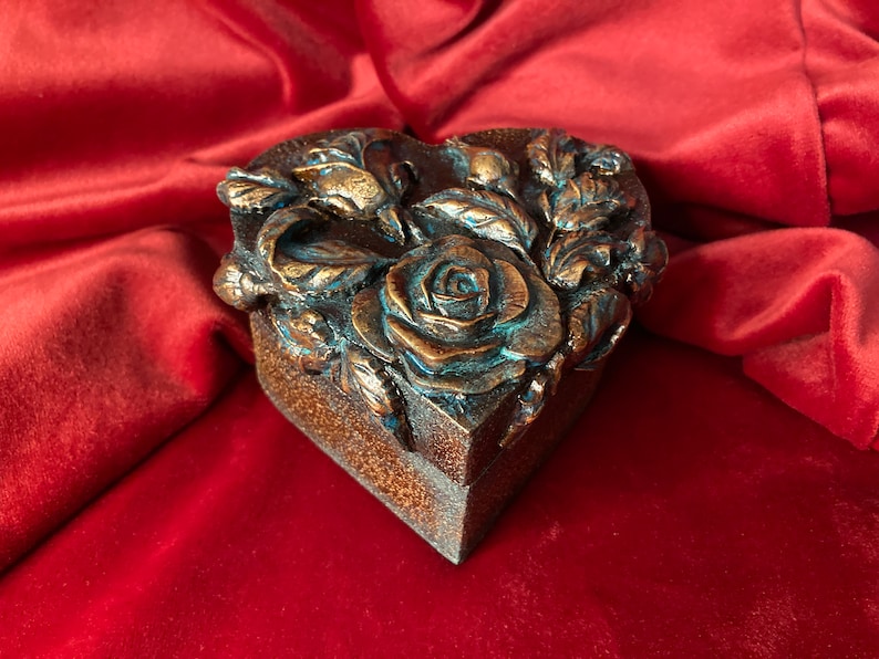 May include: A heart-shaped box with a detailed floral design. The box is made of a dark brown material and features a rose with blue accents.