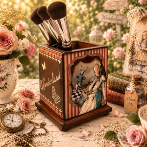 Könnte beinhalten: Ein quadratischer Make-up-Pinselhalter aus Holz mit einer Vintage-Illustration von Alice im Wunderland, die ein Mädchen und einen Hasen zeigt. Die Seite zeigt das Wort Wonderland in Schreibschrift mit Schmetterlingen, die Vorderseite einen rot-weiß gestreiften Rahmen.