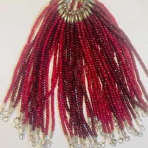 Może przedstawiać: Grupa 25 czerwonych naszyjników z koralików z kamieni szlachetnych ze srebrnymi zapięciami. Każdy naszyjnik ma około 45 cm długości.