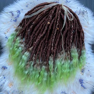 Puede incluir: Dreadlocks marrones y verdes con efecto degradado. Las rastas son de color marrón oscuro en la parte superior, pasando a un verde vibrante en los extremos. Cintas blancas y cuentas decorativas están tejidas en las rastas.