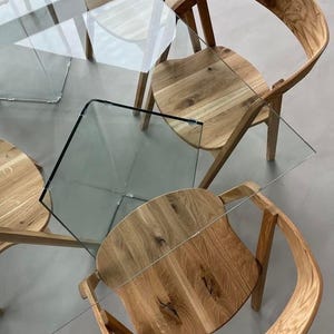 K&ouml;nnte beinhalten: Draufsicht auf ein modernes Esszimmer-Set. Das Set umfasst vier Holzst&uuml;hle mit geschwungenen R&uuml;ckenlehnen und Sitzen, kombiniert mit einem Tisch mit Glasplatte. St&uuml;hle und Tisch haben eine nat&uuml;rliche Holzoberfl&auml;che.