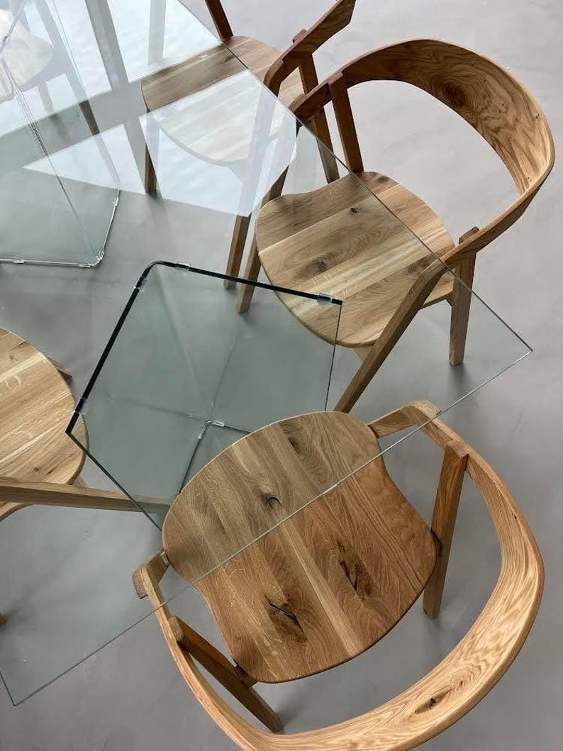 K&ouml;nnte beinhalten: Draufsicht auf ein modernes Esszimmer-Set. Das Set umfasst vier Holzst&uuml;hle mit geschwungenen R&uuml;ckenlehnen und Sitzen, kombiniert mit einem Tisch mit Glasplatte. St&uuml;hle und Tisch haben eine nat&uuml;rliche Holzoberfl&auml;che.