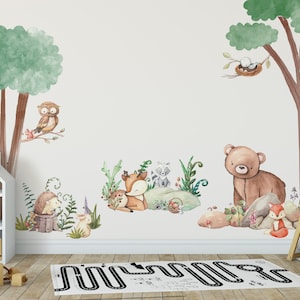 Könnte beinhalten: Eine weiße Wand mit einem Wandaufkleber zum Thema Wald, der einen Braunbären, einen Fuchs, ein Reh, eine Eule, einen Igel und ein Vogelnest zeigt. Der Aufkleber ist von einem grünen Baum, einem weißen Puppenhaus und einem Holz-Tipi umgeben.