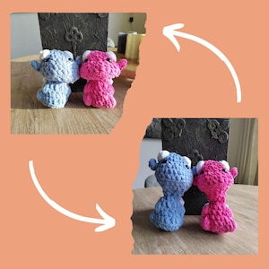 May include: Two crocheted stuffed animals, one blue and one pink, with white accents. The animals are sitting on a wooden surface.