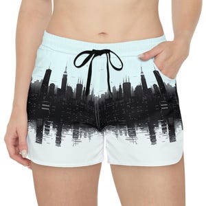 Può includere: Pantaloncini azzurri con un design di skyline in bianco e nero. I pantaloncini hanno un girovita con coulisse e un laccio nero. Lo skyline presenta edifici alti e un effetto di riflesso.
