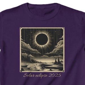 Puede incluir: Una camiseta morada con una ilustración detallada de un eclipse solar. El gráfico muestra un sol oscuro rodeado por una corona brillante, con un paisaje debajo. El texto "Solar eclipse 2025" está impreso en la parte inferior.