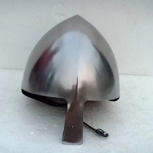 May include: A polished, silver-colored medieval helmet with a pointed top and a face guard. The helmet is made of metal and has a smooth, reflective surface. The helmet is designed to protect the head and face.