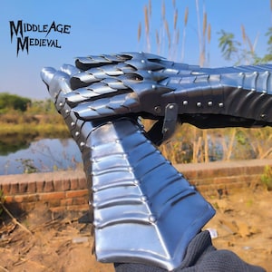 May include: A close-up of a medieval gauntlet made of shiny, riveted metal. The gauntlet is silver and has a segmented design, with overlapping plates for flexibility. The text "MIDDLE AGE MEDIEVAL" is in the upper left corner.