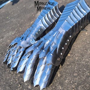 May include: Two silver-colored gauntlets with articulated plates and pointed edges, designed for medieval armor. The gauntlets are made of metal and feature rivets. The text "Middle Age Medieval" is visible in the upper left corner.
