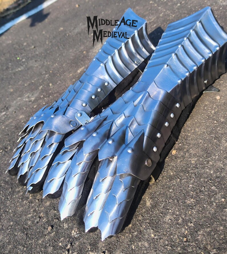 May include: Two silver-colored gauntlets with articulated plates and pointed edges, designed for medieval armor. The gauntlets are made of metal and feature rivets. The text "Middle Age Medieval" is visible in the upper left corner.